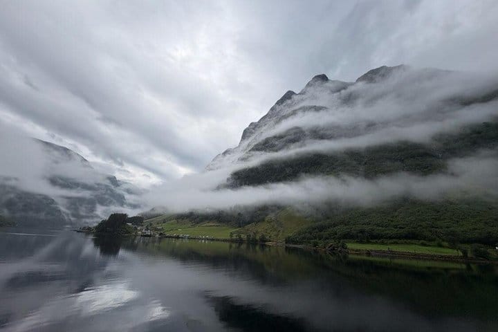 Low clouds wrapping mountains reflected in still Nærøyfjord water