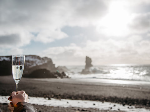 A hand is reached towards the sea, as in a toast, on the black sand beaches of Djúpalónssandur