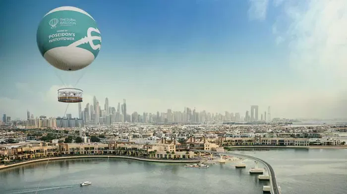 An aerial view shows a tethered balloon floating above coastal buildings and a city skyline at The Dubai Balloon at Atlantis.