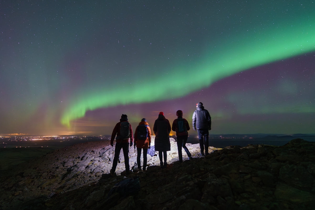 5 travelers holding flashlights while gazing up at the night sky that is filled with the Northern Lights