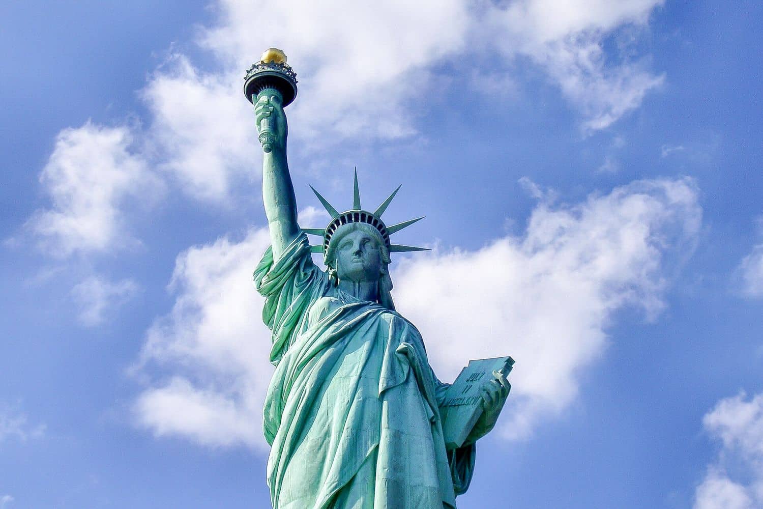 Statue of Liberty torch and crown against blue sky with clouds