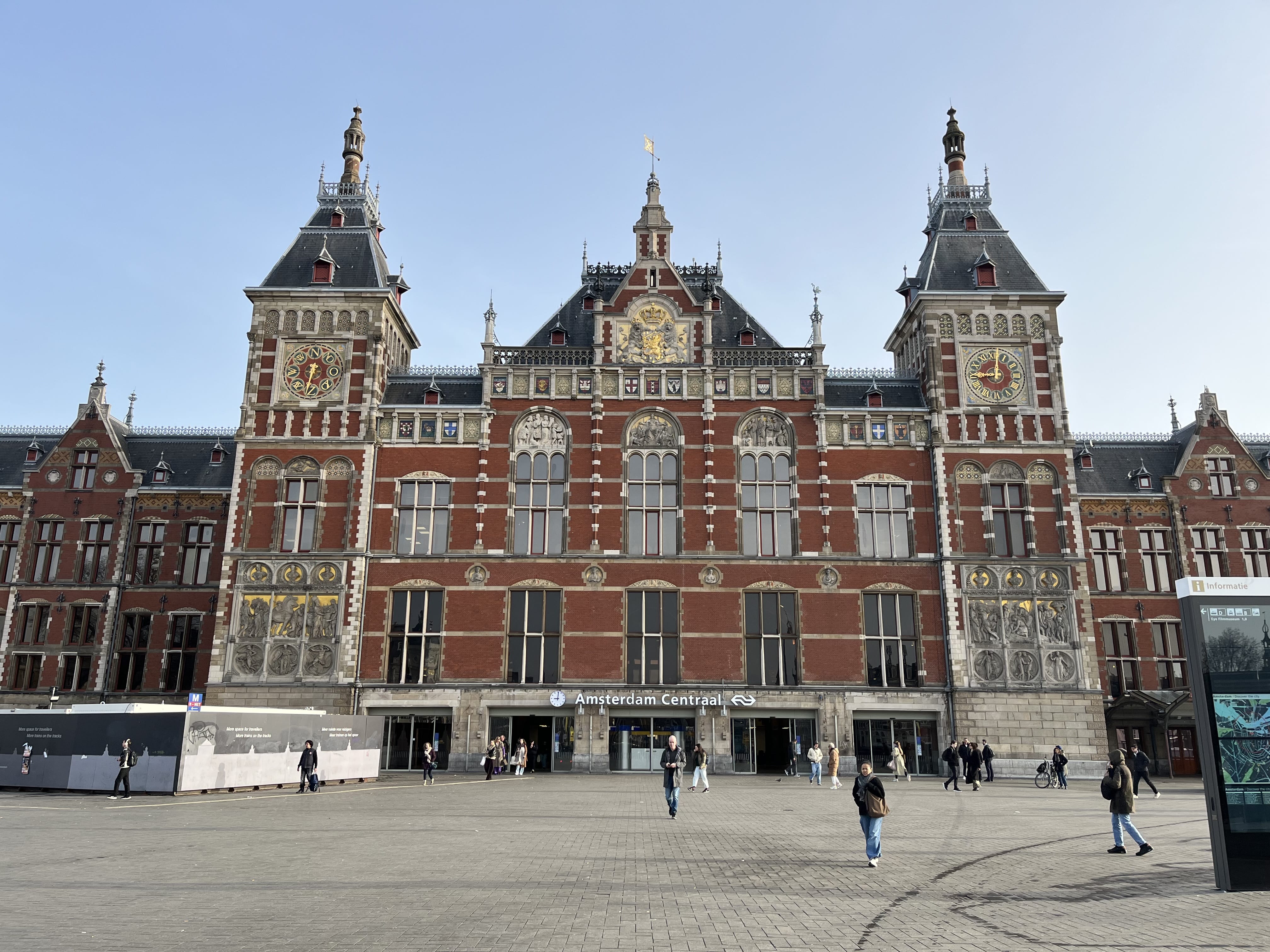 The historic Amsterdam Central Station building with twin towers and ornate brick architecture, viewed from the open square