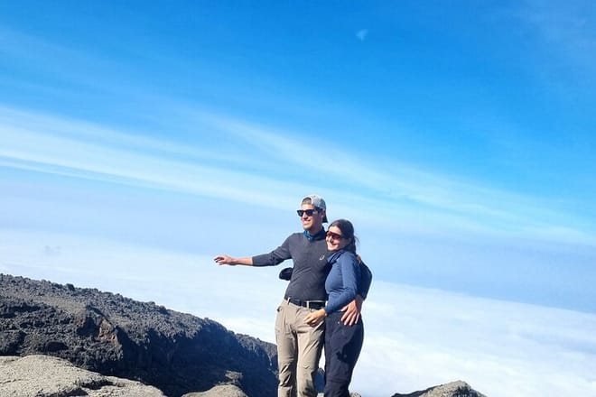  A couple standing together and embracing on a high-altitude rocky ridge of Mount Kilimanjaro, surrounded by a sea of clouds.