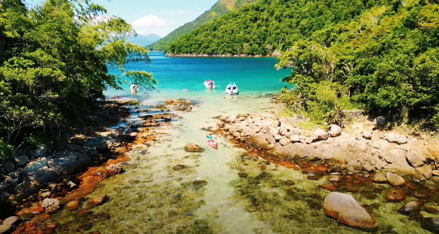 View of a serene bay at Lagoa Verde, Ilha Grande, with turquoise waters, lush green hills, boats, and people swimming and kayaking near the 