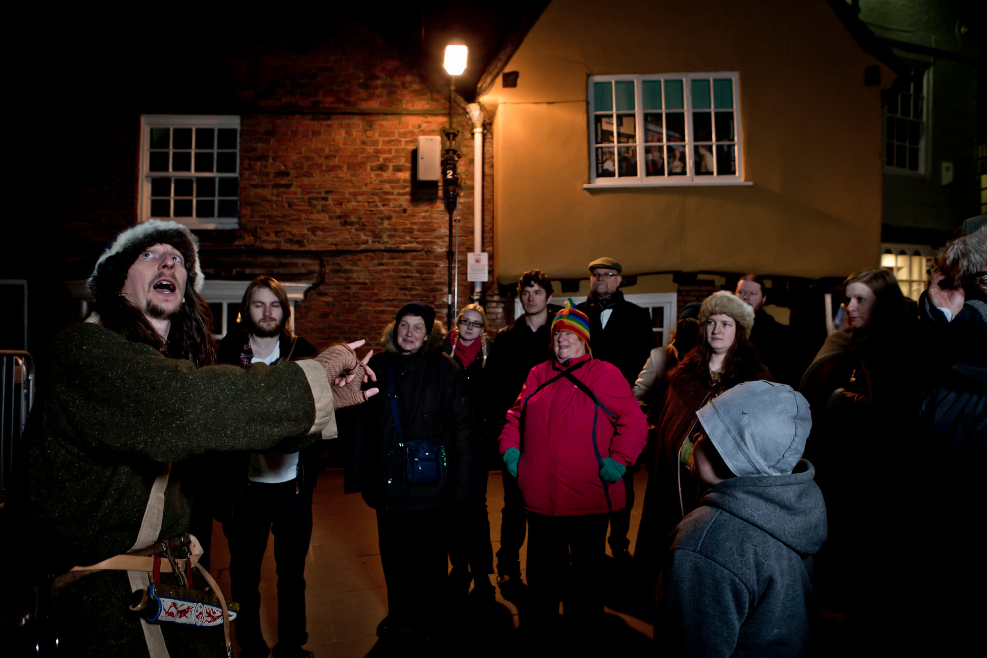 A costumed Viking tour guide with a crowd at King's Square, at night.