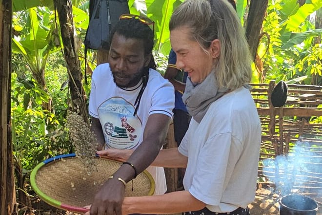 A local guide and a tourist using a traditional woven tray to winnow coffee beans in a sunlit garden.