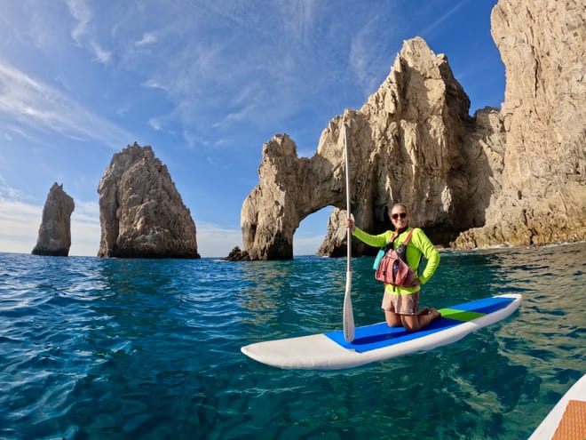 Woman paddle boarding near El Arco rock formation in Cabo San Lucas with clear turquoise water