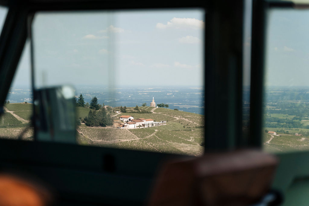 From inside a vintage Land Rover, view outside the window of the Beaujolais countryside landscape, with a village, vineyards and a church