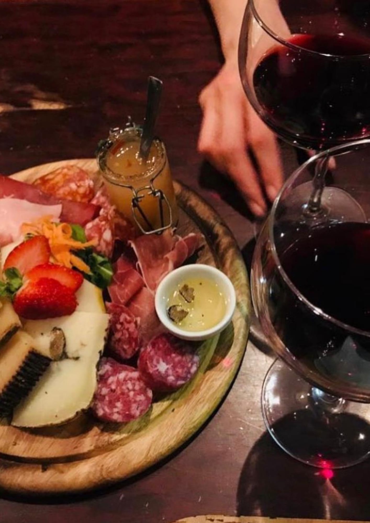 A rich plate of cheeses and cured meats, with deep red wine — a slow, flavorful pause in a Roman wine bar.