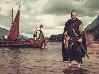 Viking Warrior armed with a sword standing close to a ship.