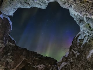 View looking upward through a collapsed opening in the roof of Vidgelmir lava cave, framed by ice-encrusted volcanic rock, with the northern