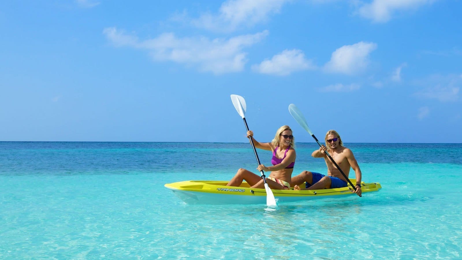 A couple kayaking together in the calm waters of Himmafushi Lagoon, surrounded by clear blue skies and tranquil surroundings