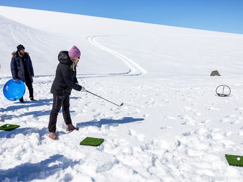 person playing golf ontop the glacier, standing in white snow