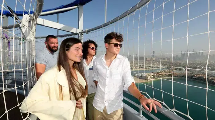 Four people stand on the observation deck behind safety netting, looking out at the distant coastal view from the high vantage point at The Dubai Balloon at Atlantis.