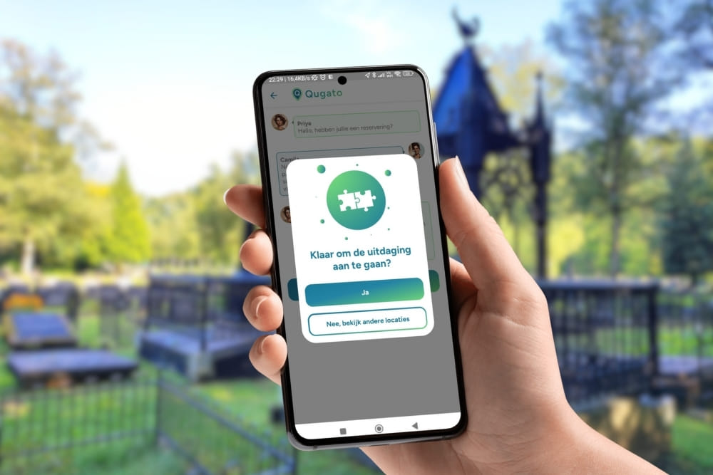 Phone showing the app interface of the Assen City Detective game in front of Noorderbegraafplaats