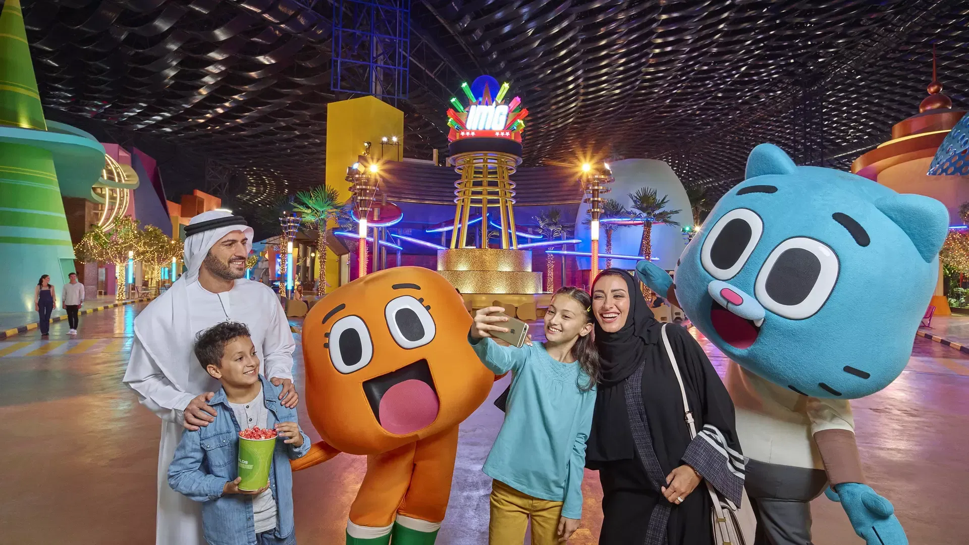 A family poses for a selfie with large costumed characters in an indoor plaza at IMG Worlds of Adventure Theme Park.