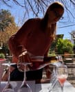 A lady is pouring Champagne into glasses outside in the courtyard