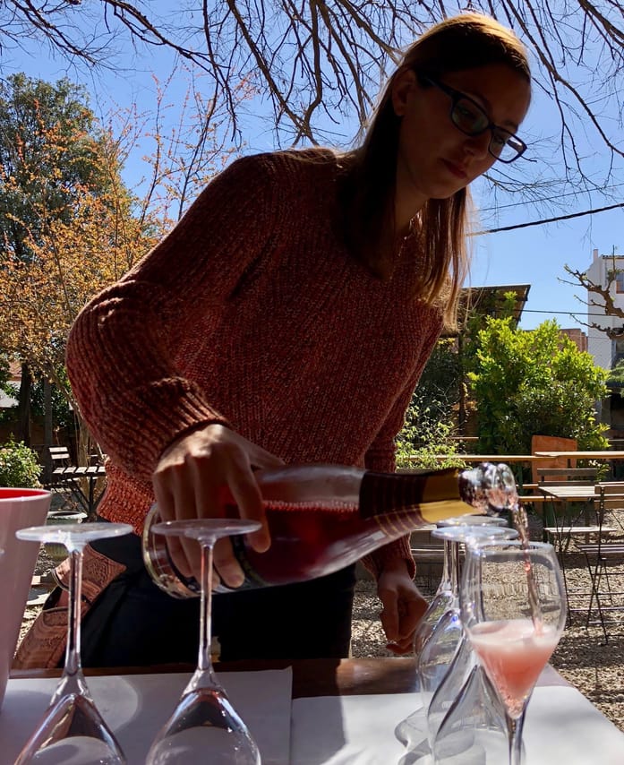 A lady is pouring Champagne into glasses outside in the courtyard