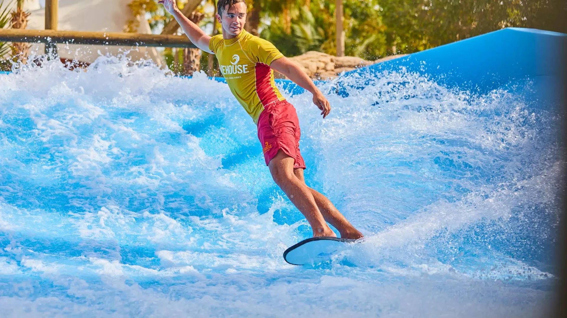 A man in a yellow rash vest standing upright on a flowboard on the FlowRider surf wave at Aquaventure Waterpark