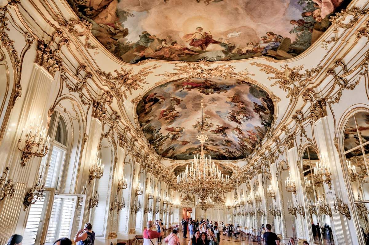 Interior of the Grand Hall in Schönbrunn Palace, Vienna, with ornate chandeliers, gilded details, and vivid ceiling frescoes