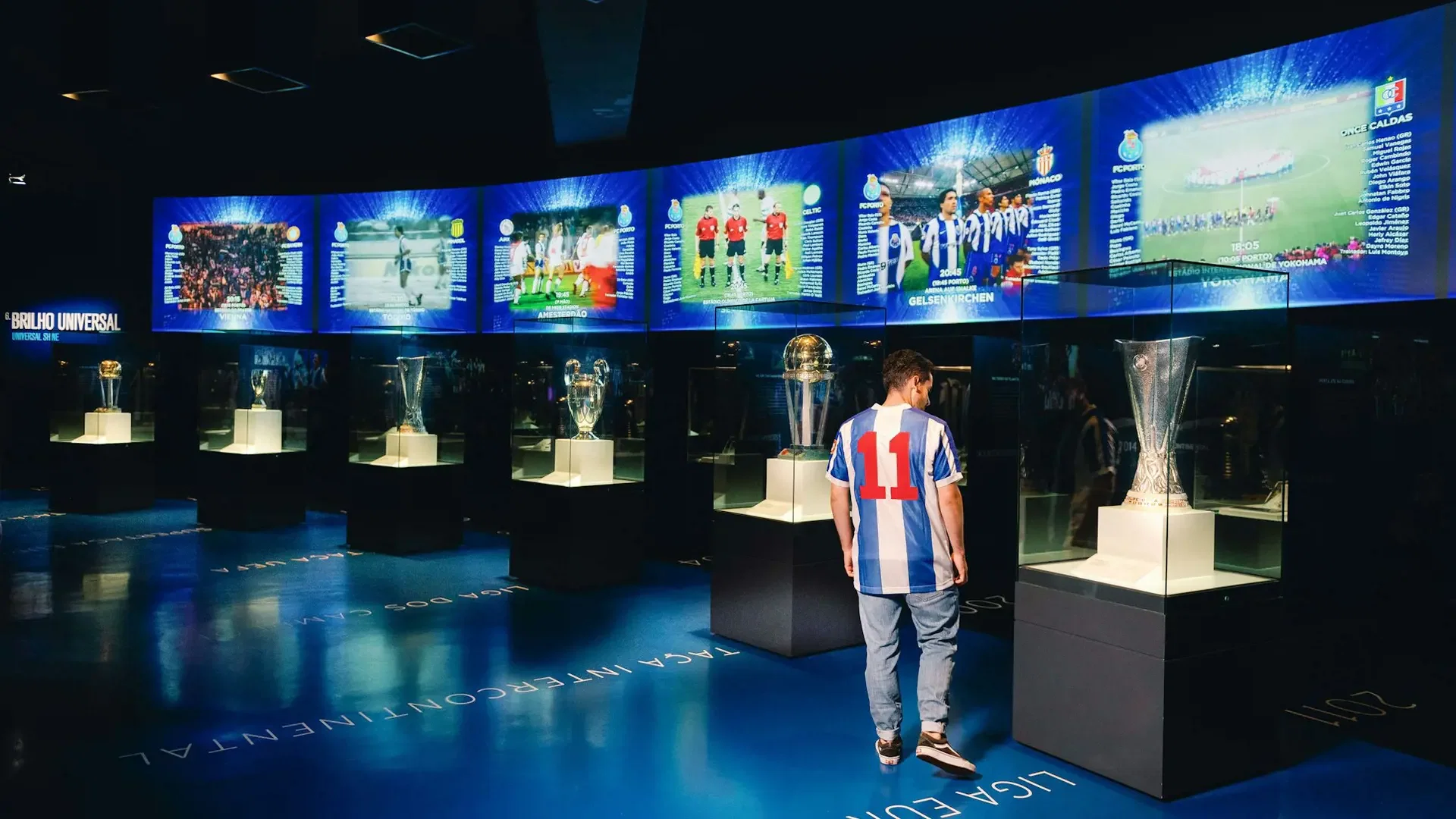 A visitor stands before illuminated trophy cases and large video screens in a dark gallery at FC Porto Museum & Dragão Stadium ticket.