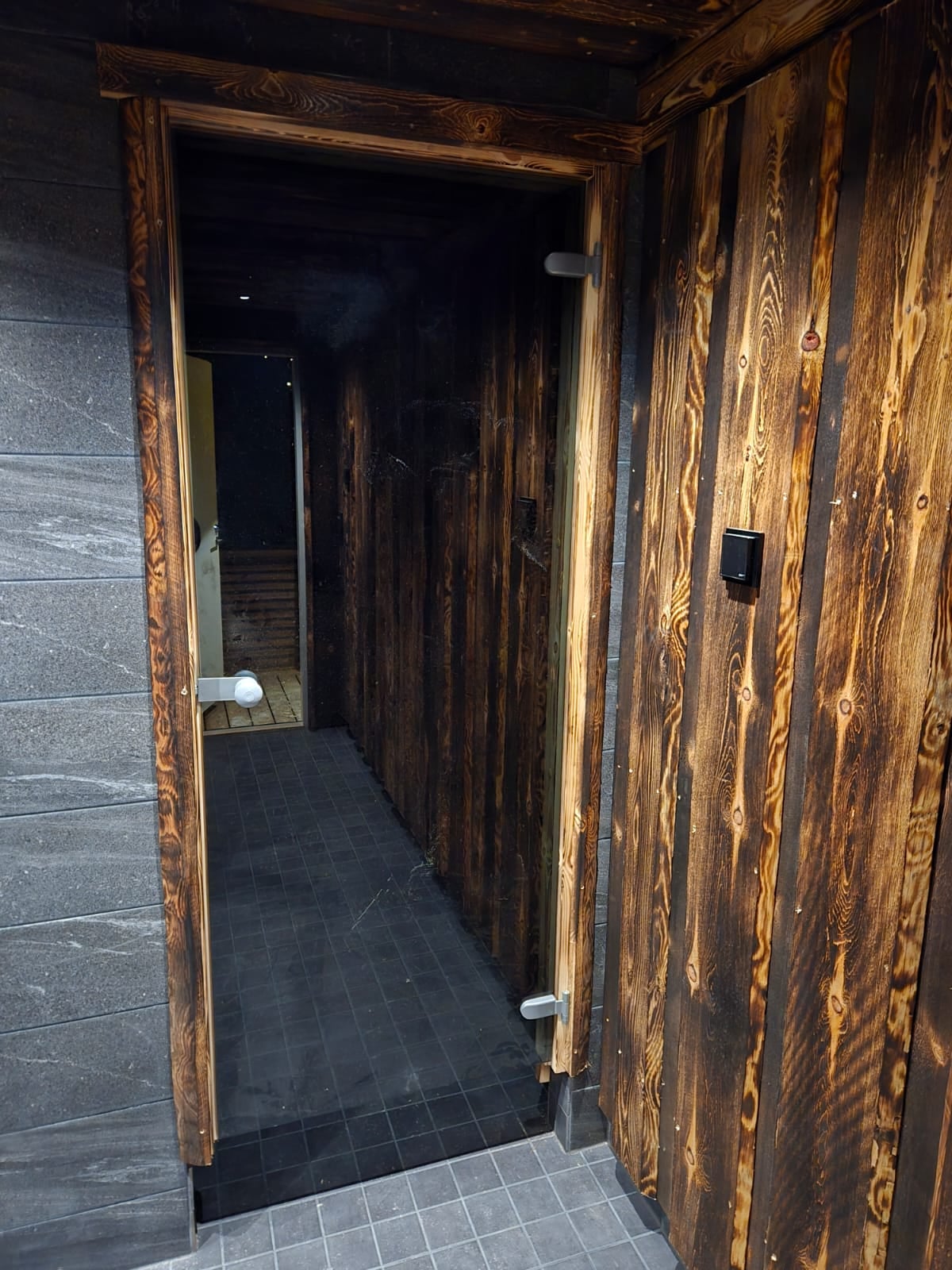 Black glass door leading to the private shower and sauna facilities with dark Finnish timber walls