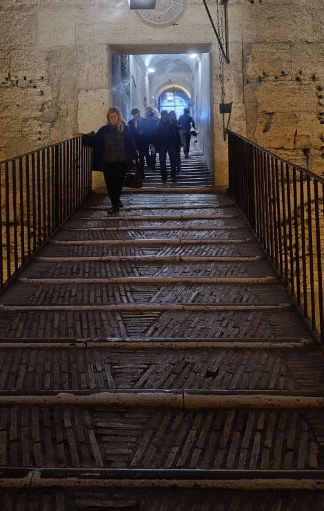 Follow the worn steps upward, with stone walls close by and Rome’s history rising around you.