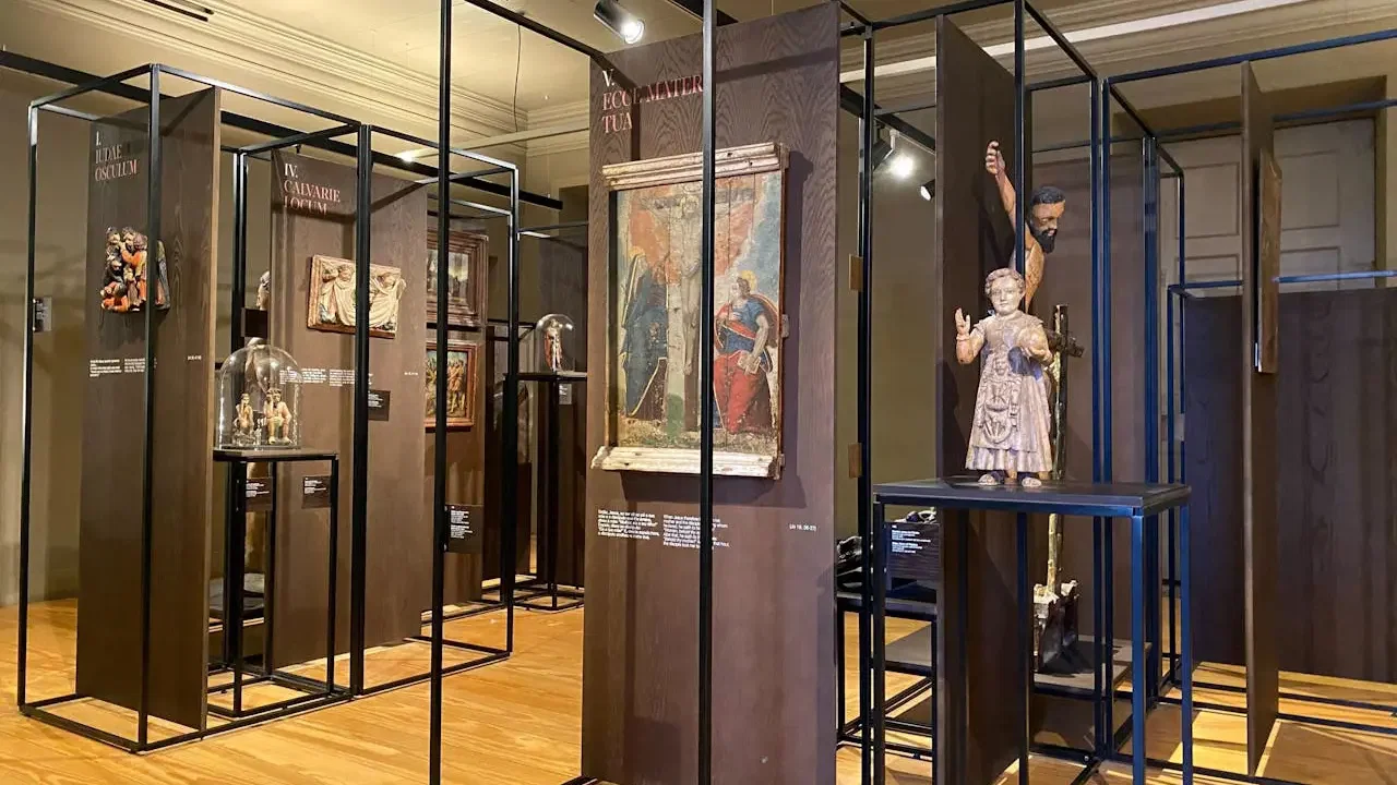 An exhibition space features dark wooden display structures, religious art, and statues on stands over a wooden floor at Clérigos Tower & Museum Ticket.