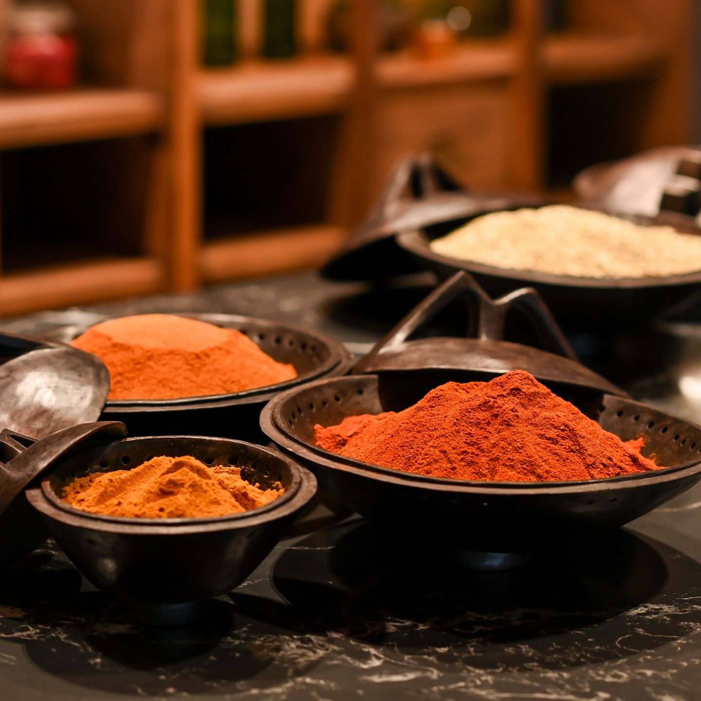 A close-up shot of several dark, rustic-style bowls filled with brightly colored spices.