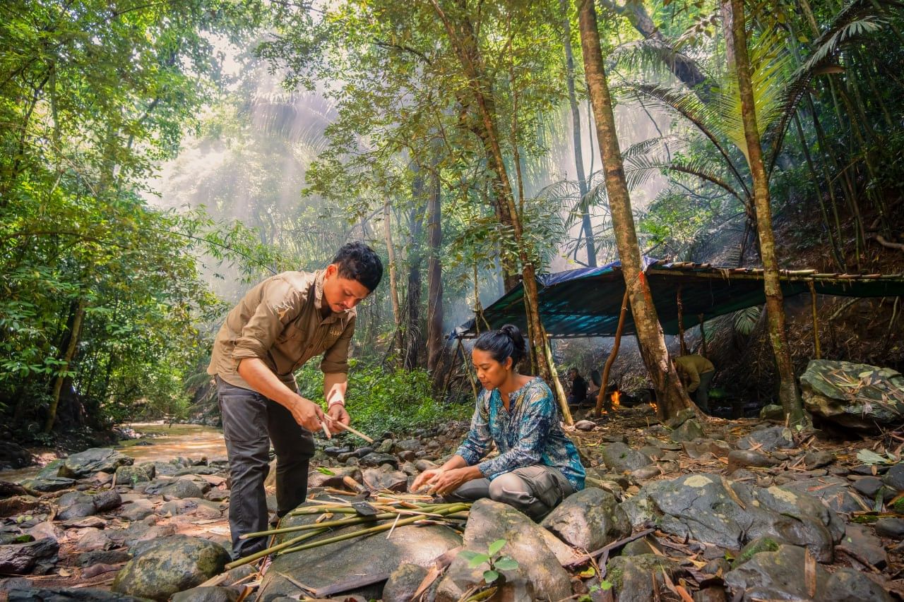 Two people preparing a Bunong soup in the forest, peeling rattan stems