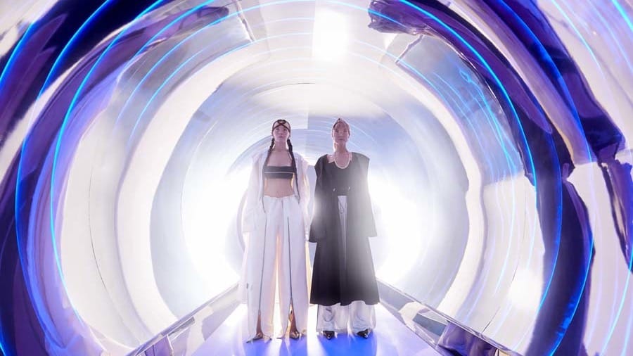 Two visitors standing inside a bright white circular tunnel ringed with blue light at AYA Universe Dubai