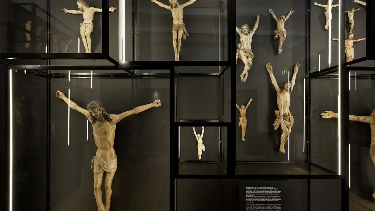 A museum display featuring multiple wooden crucifix sculptures arranged inside lit glass and black metal cases at Clérigos Tower & Museum Ticket.