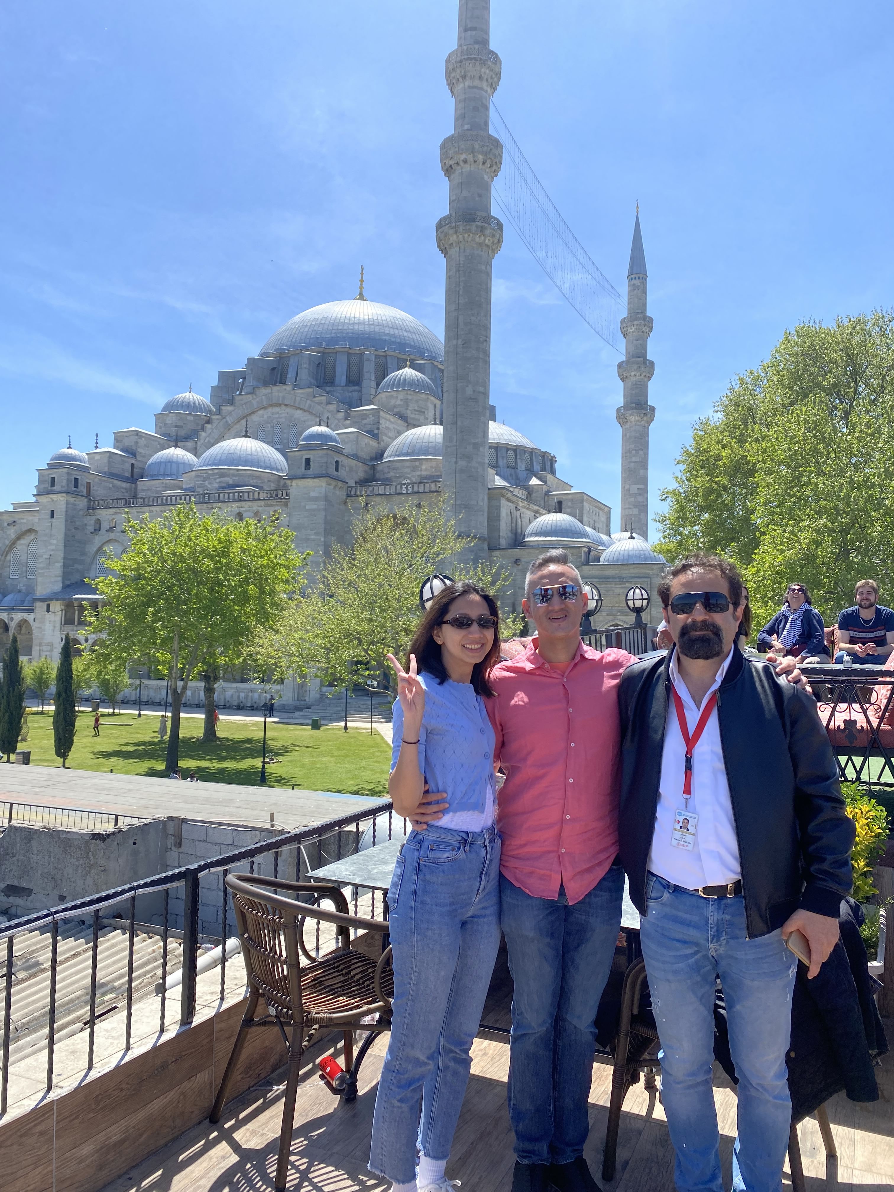 “A tour guide smiling with a happy couple posing in front of Istanbul’s Blue Mosque during their honeymoon visit.”