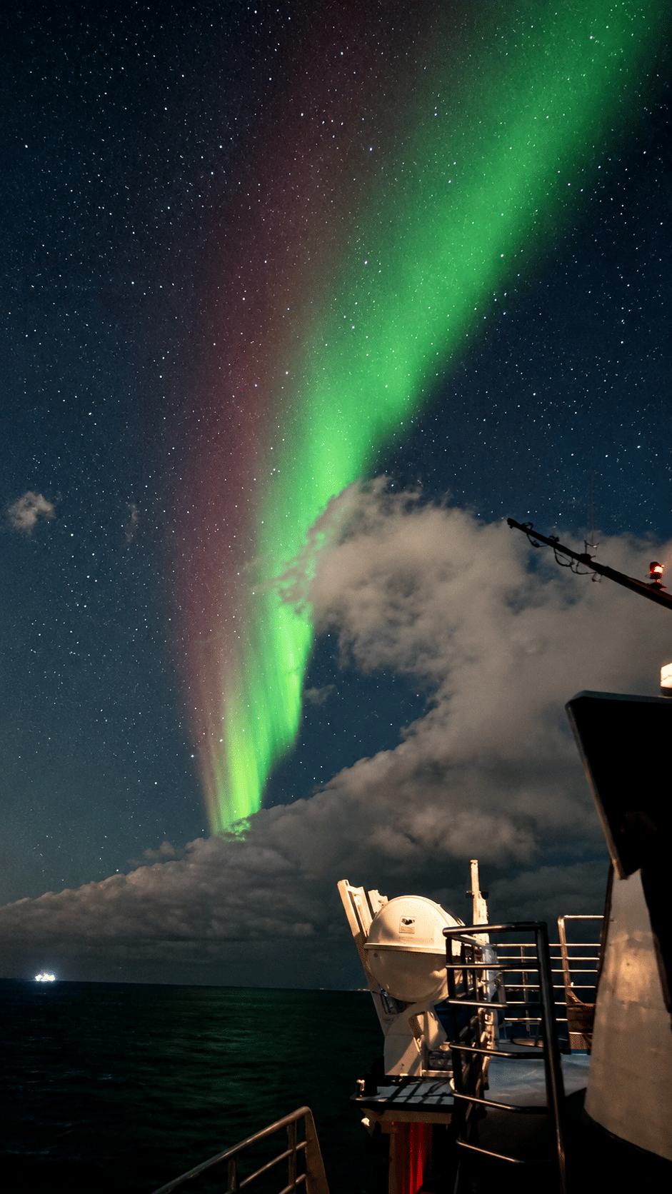 Tall green and pink aurora curtains glowing beside clouds in the night sky over Iceland.