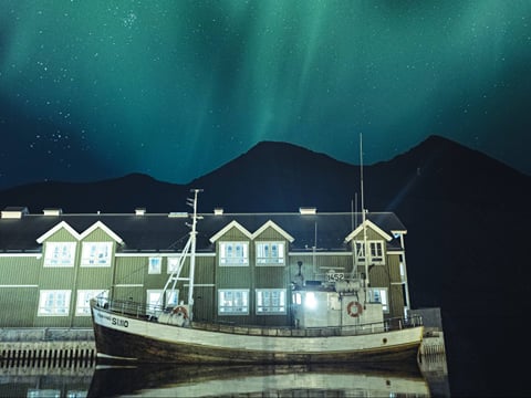 View of a boat docked, with houses behind and northern lights in the sky above
