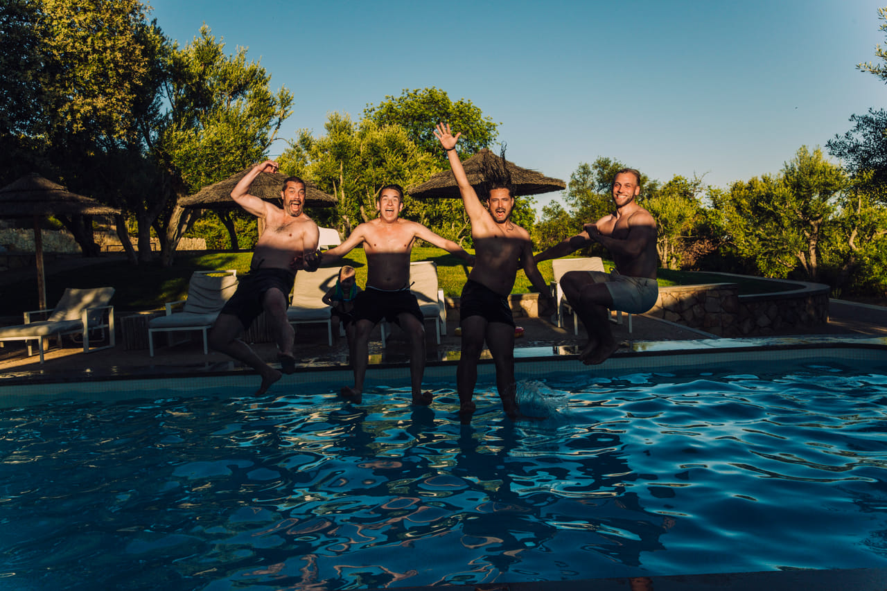A group of four boys captured mid-motion as they fall into a swimming pool together.