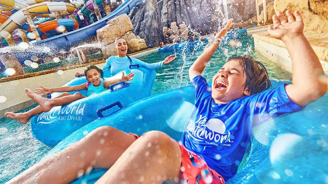 Happy children and a woman ride in blue inner tubes down a lazy river at Yas Waterworld, Abu Dhabi.