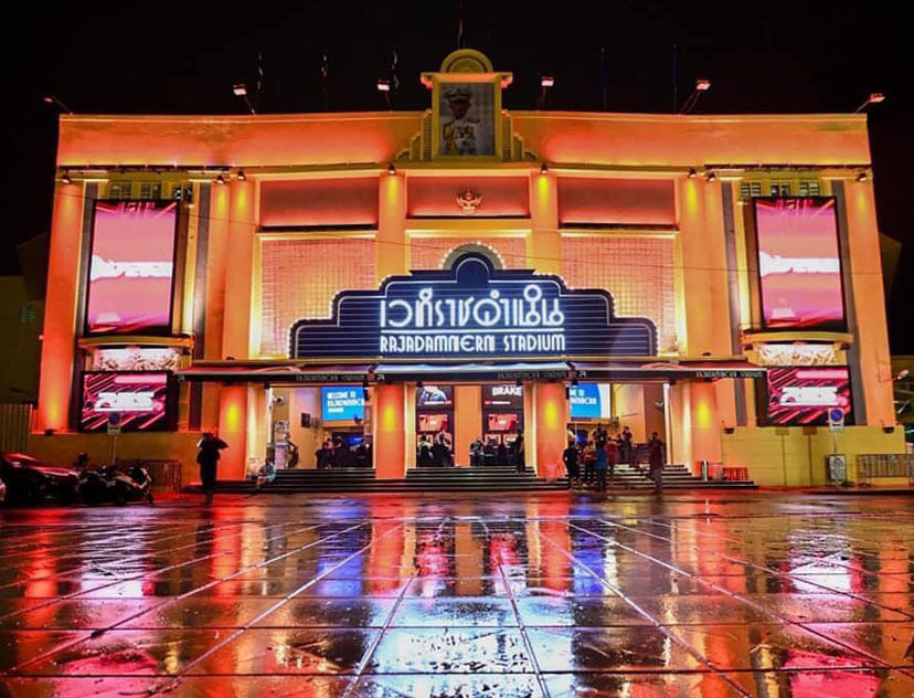 Rajadamnern Stadium Bangkok illuminated at night with reflections on wet ground, historic home of Muay Thai boxing