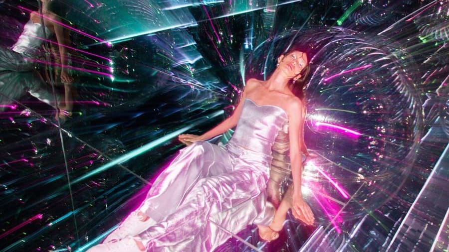 A visitor reclining inside a mirrored tunnel streaked with pink and green laser light at AYA Universe Dubai