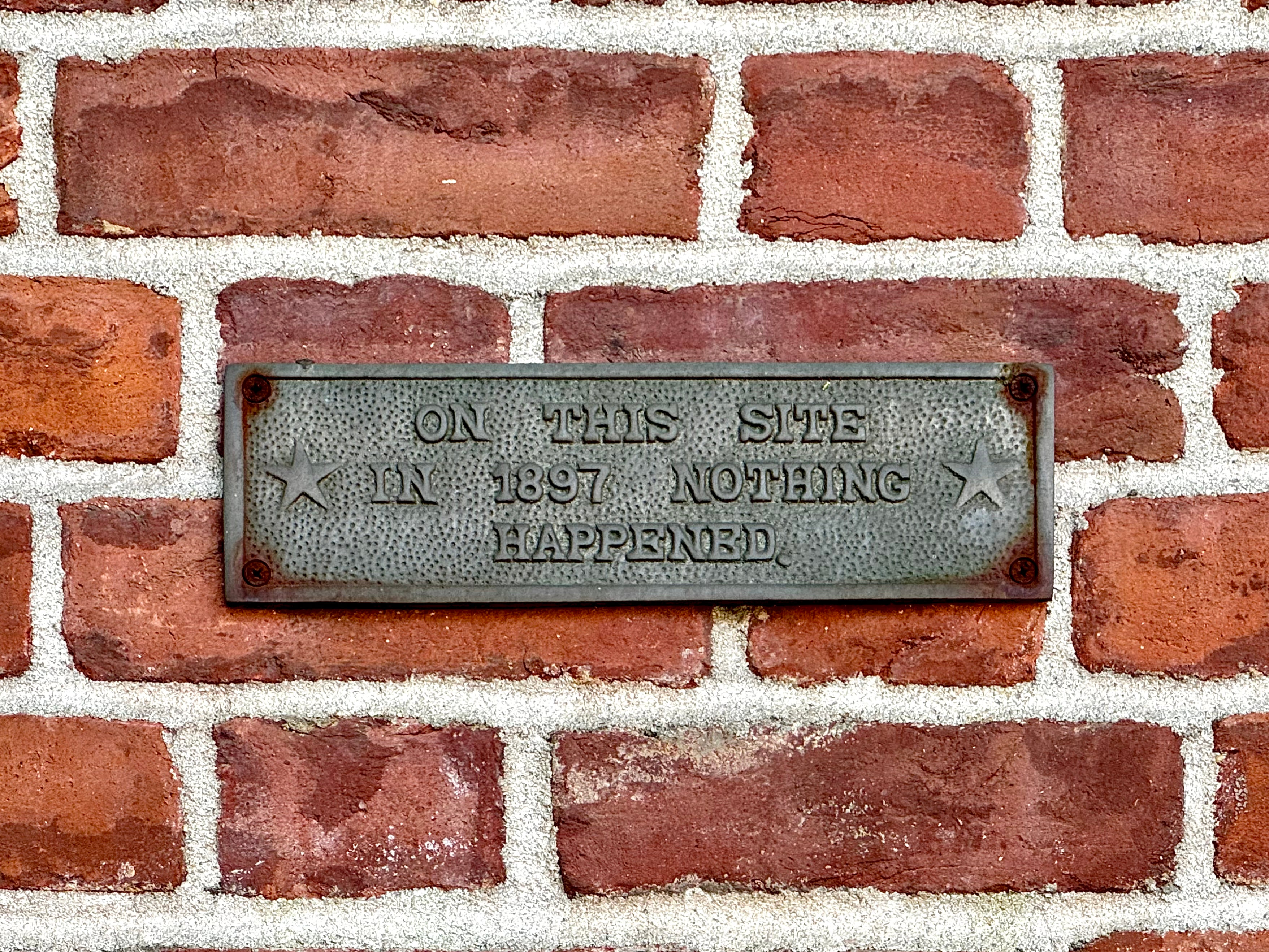 A small metal plaque on a brick wall reads, “On this site in 1897 nothing happened.”