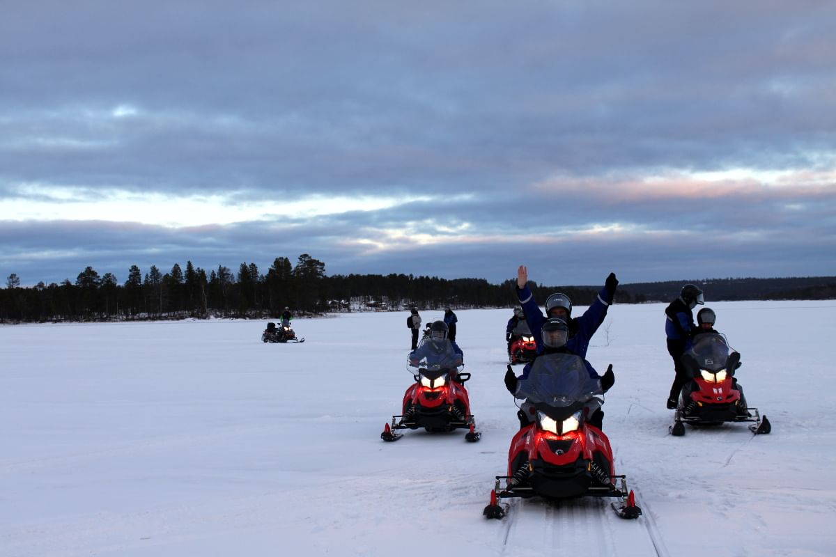 Four snowmobiles with two people in each on lake ice.