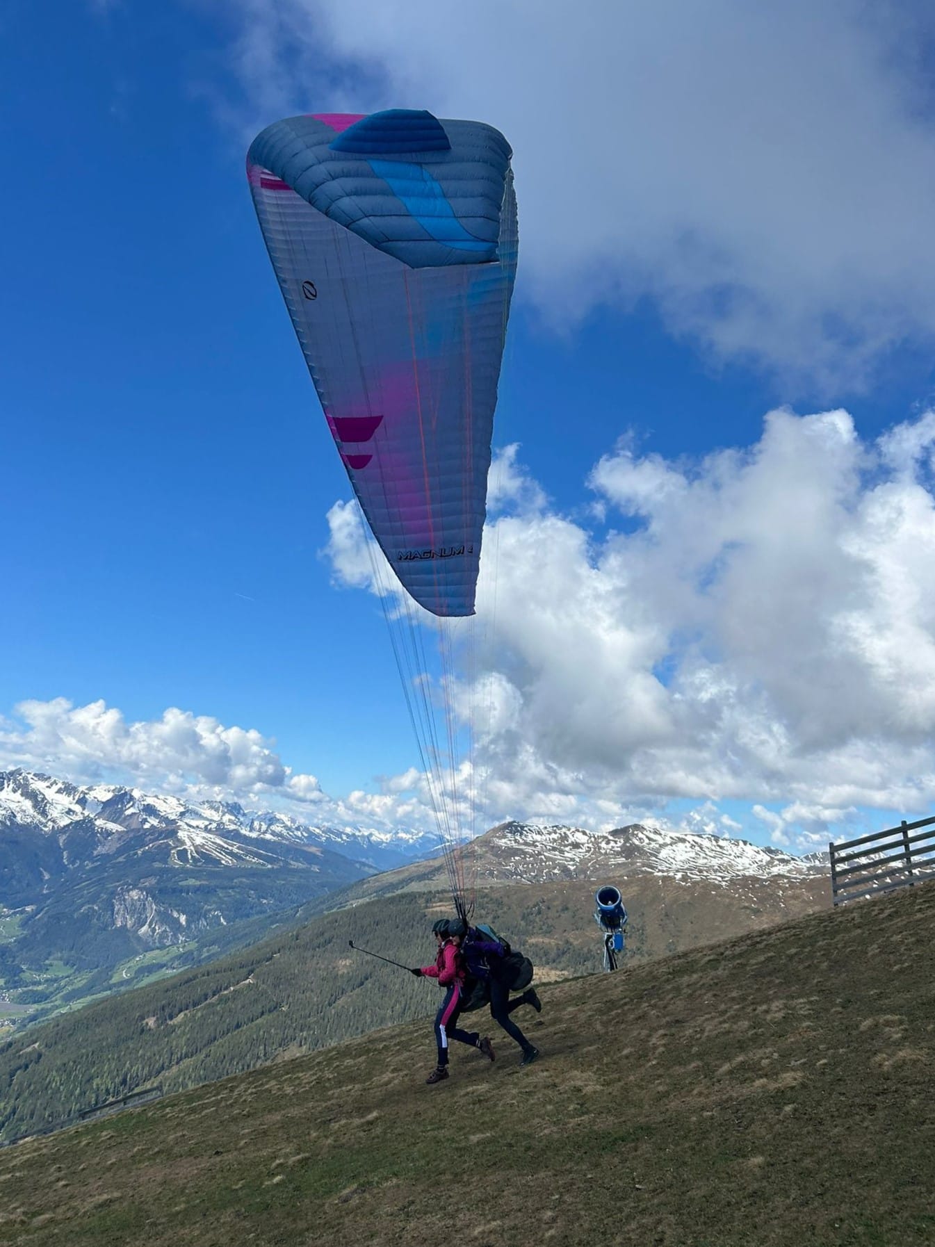 female pilot and passenger running down the hill while taking off mountains in the background