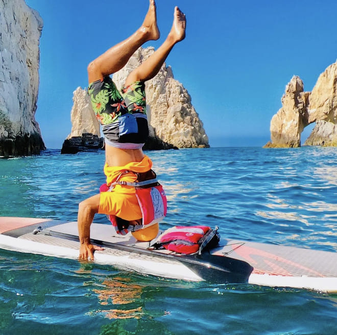 Person doing a headstand on a paddle board near El Arco in Cabo San Lucas with turquoise ocean water