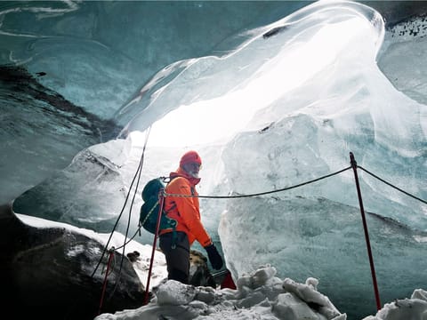 a man standing in a natural ice cave and gazing at the crystal clear wall of the ice