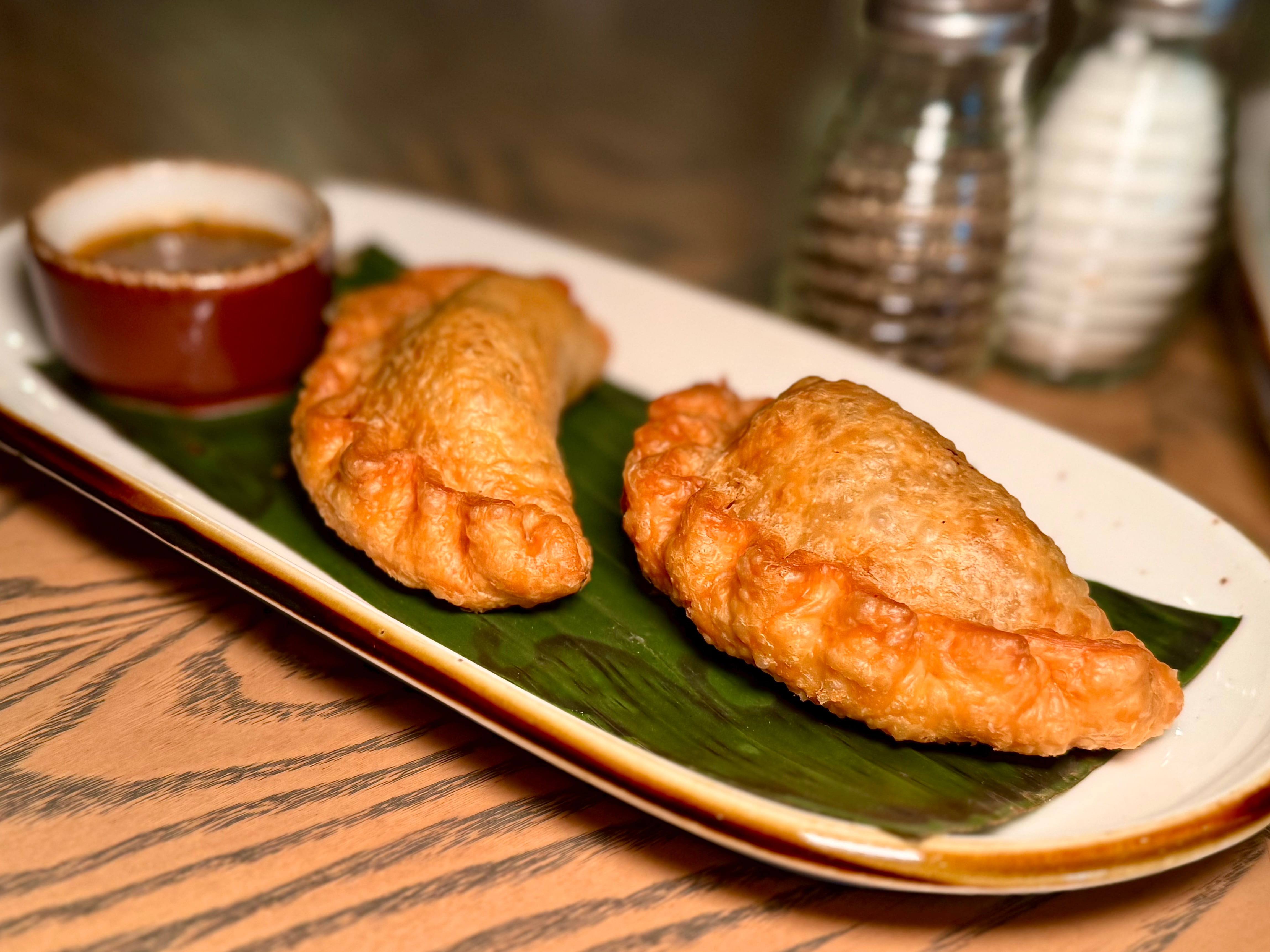 Two golden-brown empanadas served on a rectangular plate with dipping sauce.