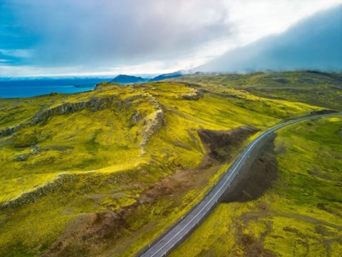 An aerial view of a long and winding road, threading its way through mountainous landscapes