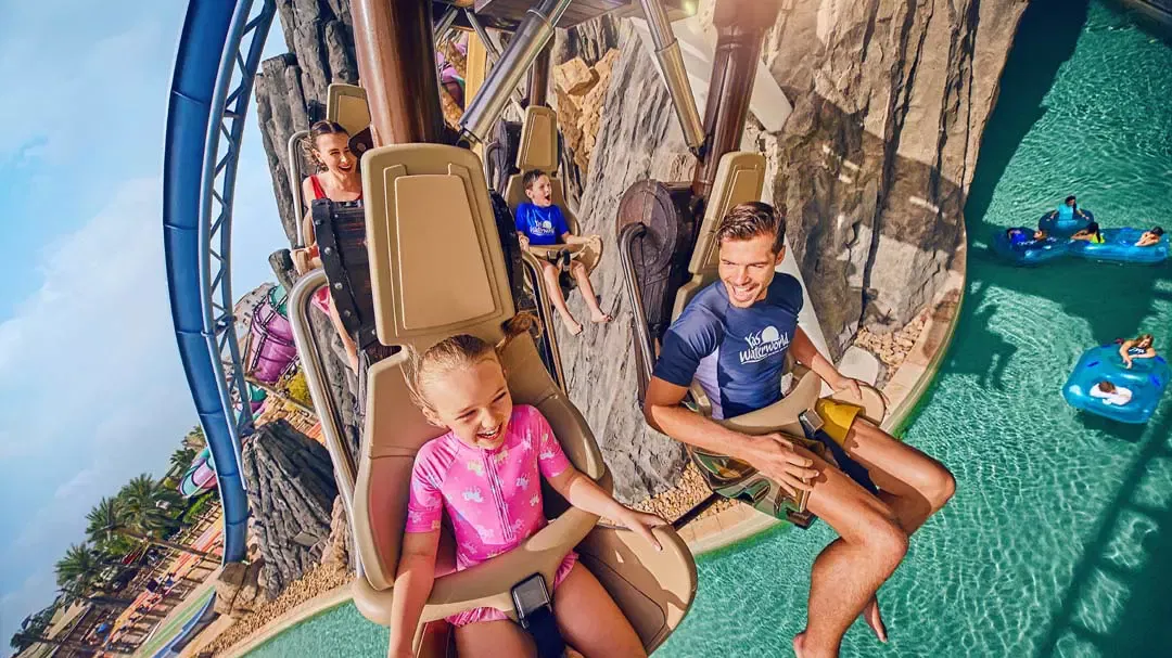 A smiling family rides in a suspended roller coaster above a swimming pool at Yas Waterworld, Abu Dhabi.