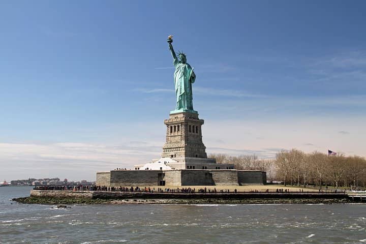Statue of Liberty on Liberty Island with visitors on the pedestal and Manhattan skyline in background
