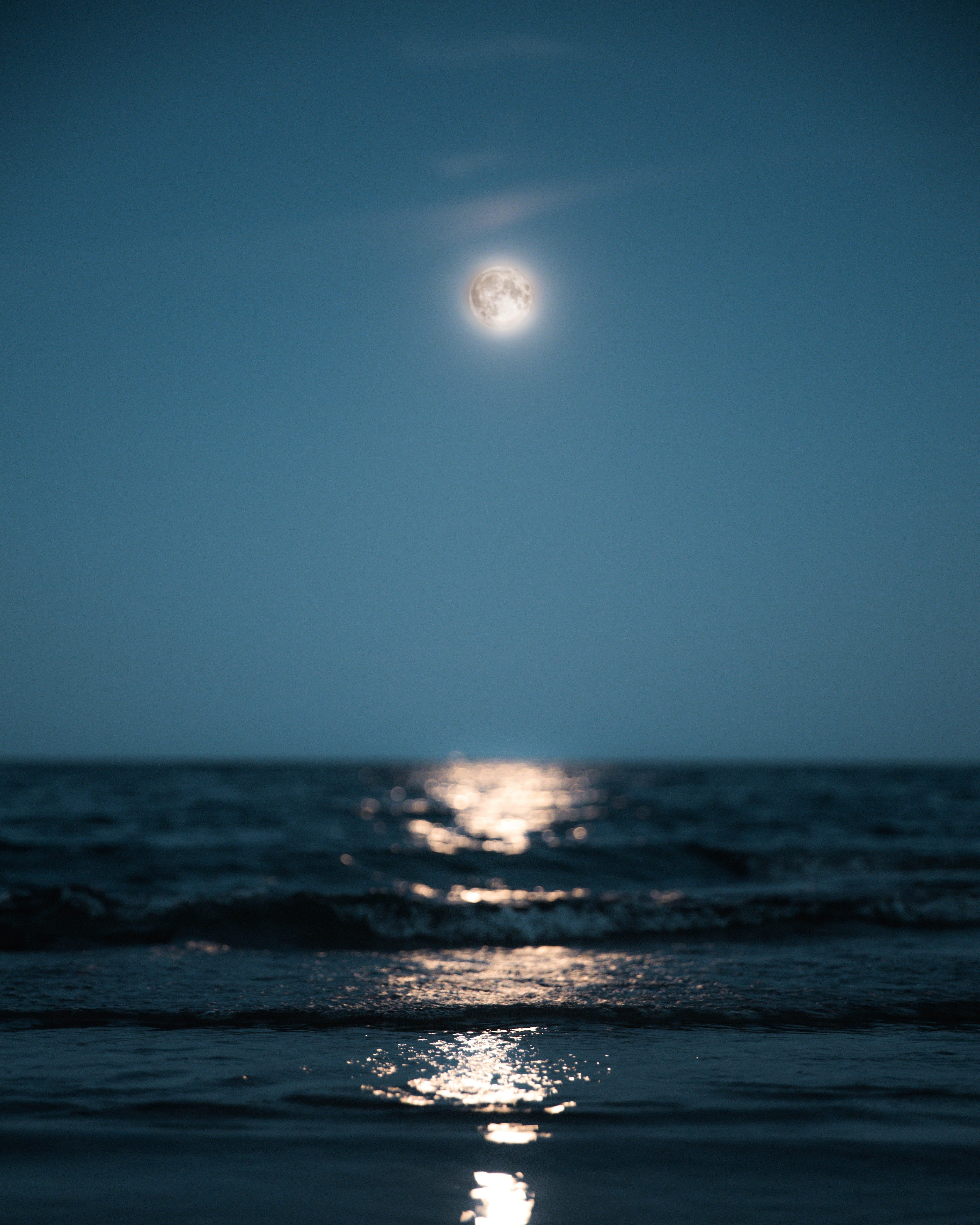 Calm sea with waves reaching the shore towards you with the wavy reflection of the full white moon