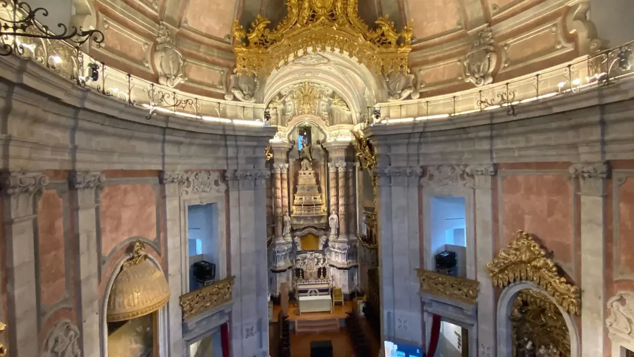 A high-angle view looking down into the ornate, pink and grey stone interior of a church with a golden altar at Clérigos Tower & Museum Ticket.